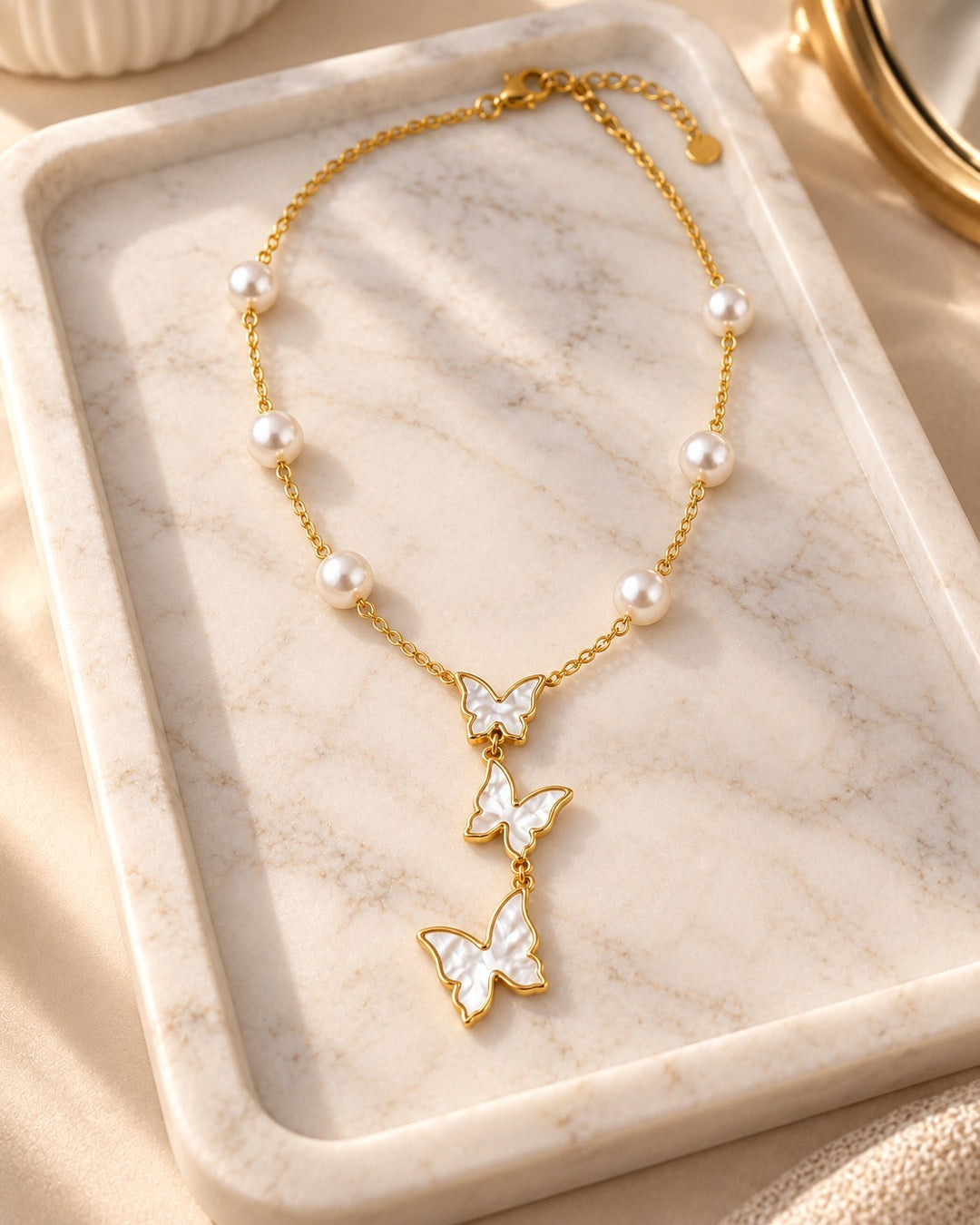 Elli Jewellery gold plated necklace featuring a delicate triple butterfly pendant and pearl accents on a marble tray.