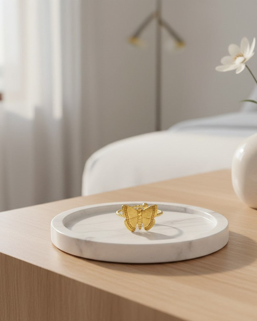 Elli Jewellery gold plated open butterfly adjustable ring resting on a white marble tray in a bright bedroom setting.