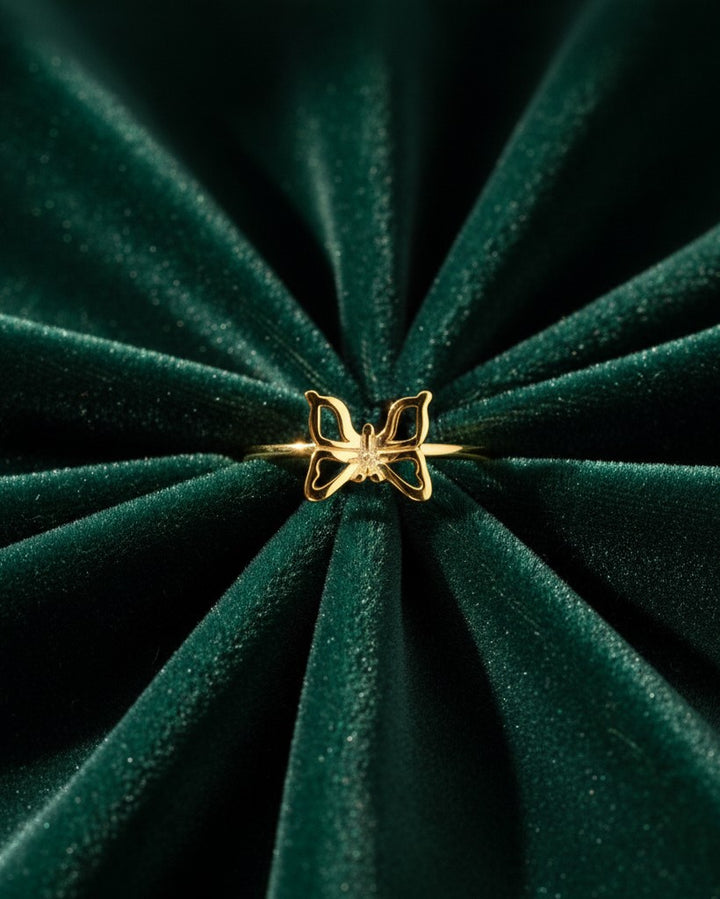 Elli Jewellery gold plated butterfly statement ring with crystal accents on a dark green velvet background