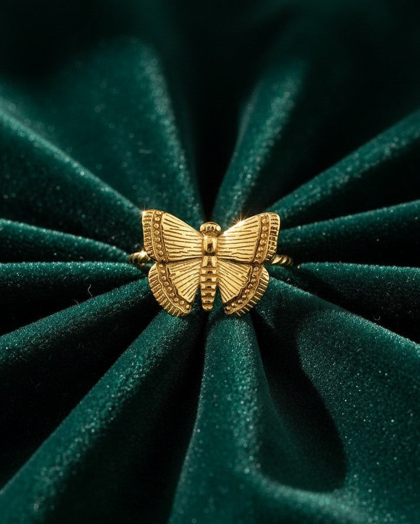 Elli Jewellery gold plated delicate open butterfly ring with textured wing details on a dark green velvet background.