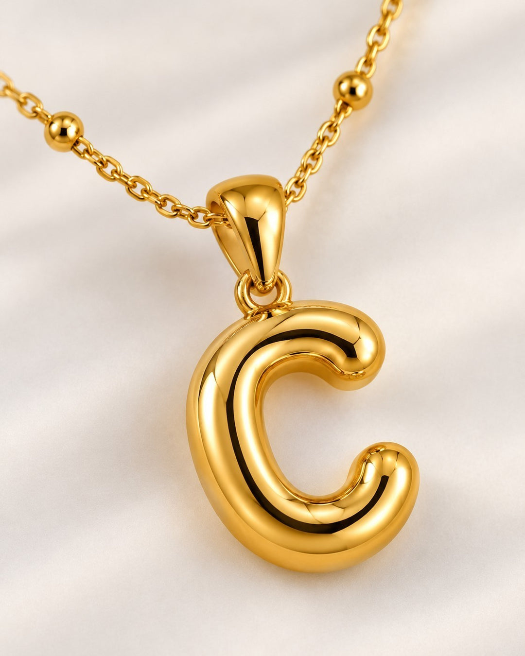 Elli Jewellery gold plated chunky C initial pendant on a delicate beaded chain against a soft white background