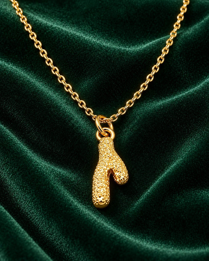Elli Jewellery gold plated stainless steel cactus pendant necklace on a delicate chain against dark green velvet.
