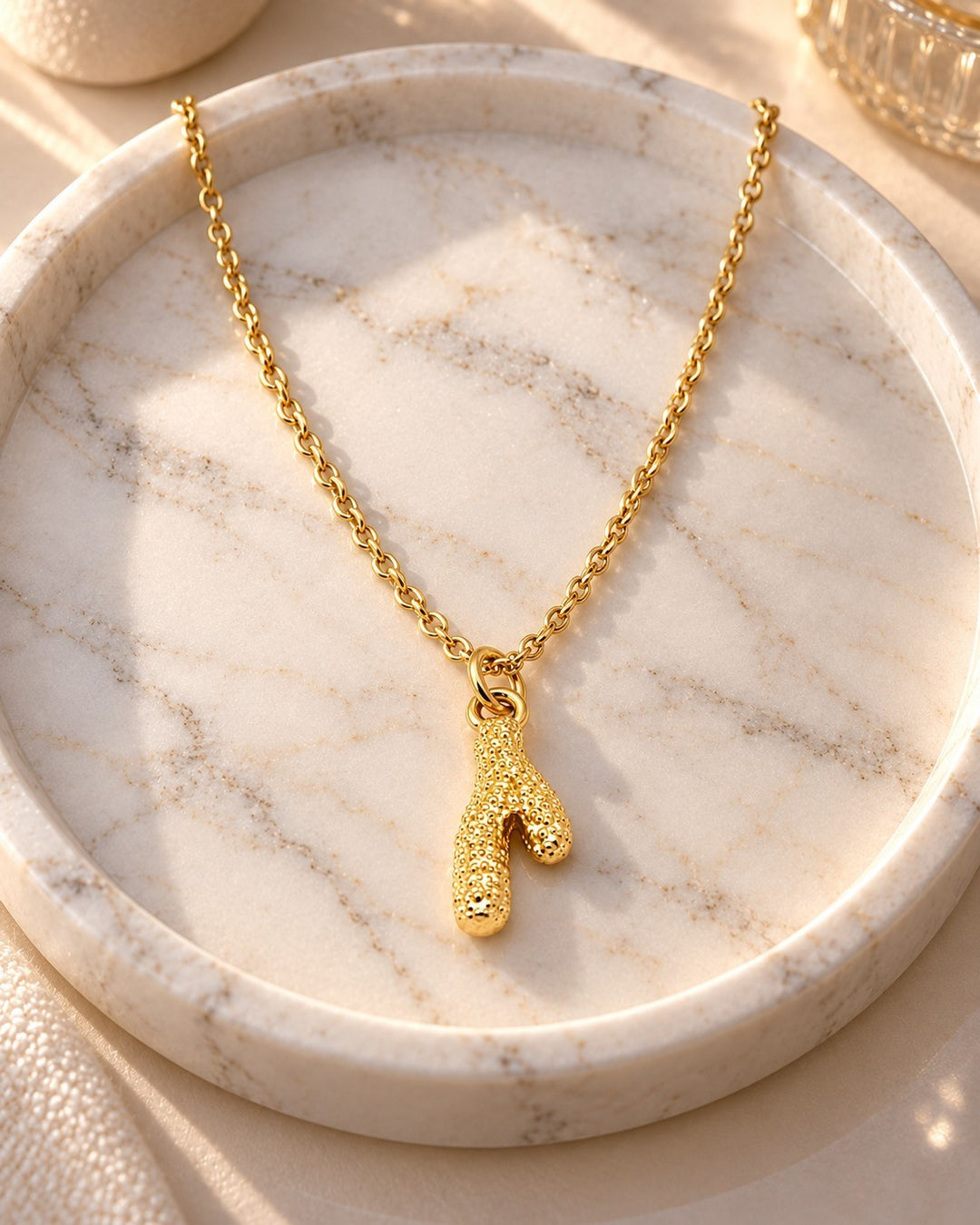 Elli Jewellery gold plated stainless steel cactus pendant necklace on a dainty chain resting on a marble tray
