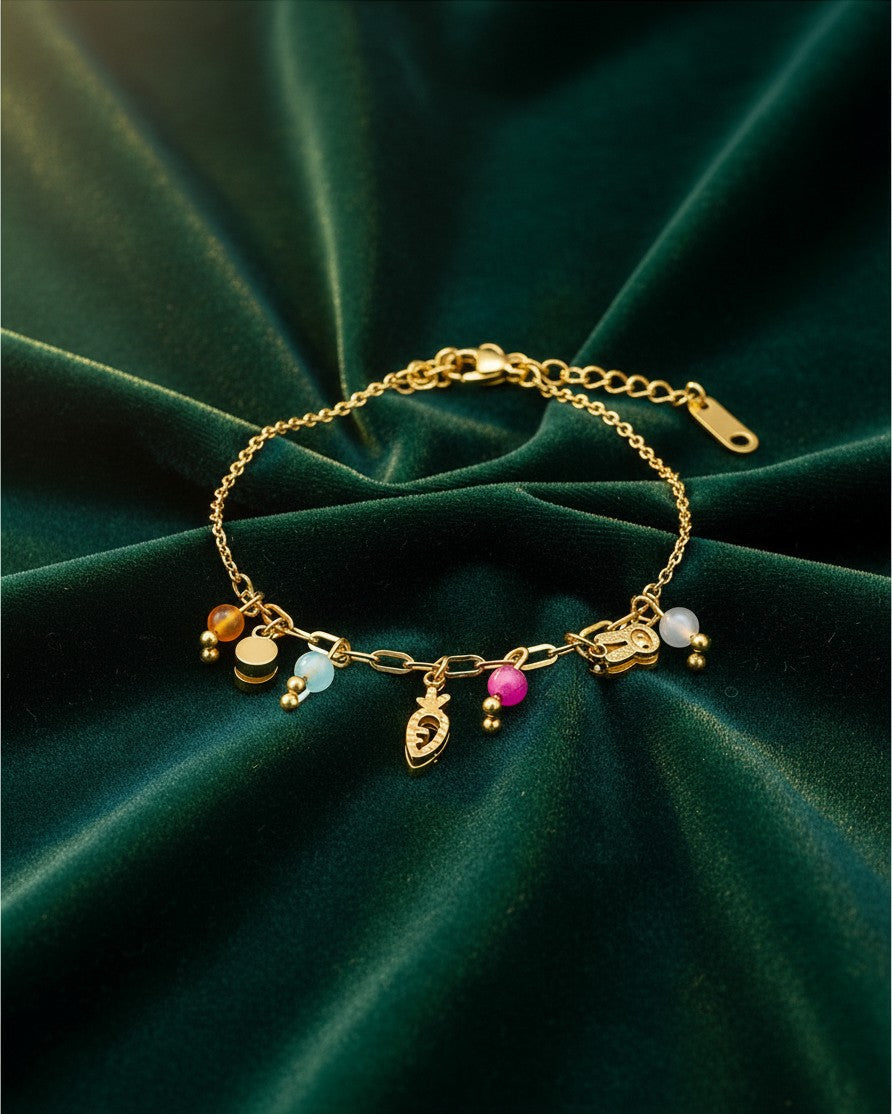 Elli Jewellery gold plated charm bracelet featuring a playful carrot charm and colorful beads on a green velvet cloth.