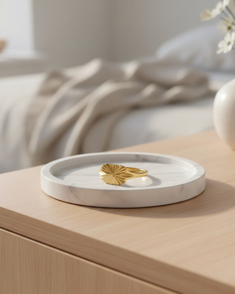 Elli Jewellery gold plated signet ring with carved geometric sunburst detail resting on a white marble tray