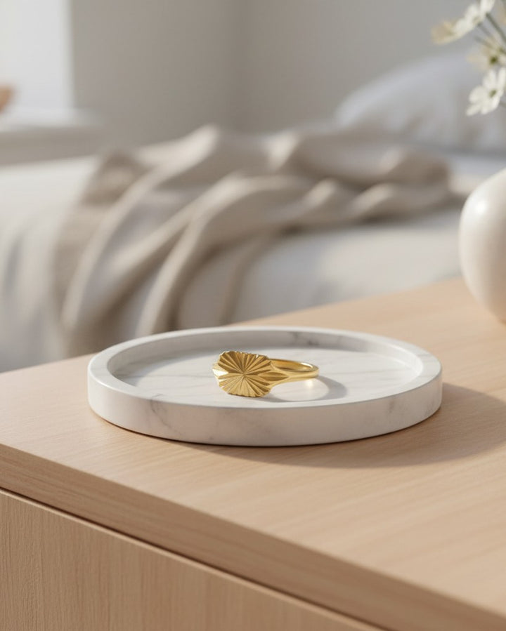 Elli Jewellery gold plated signet ring with carved geometric sunburst detail resting on a white marble tray