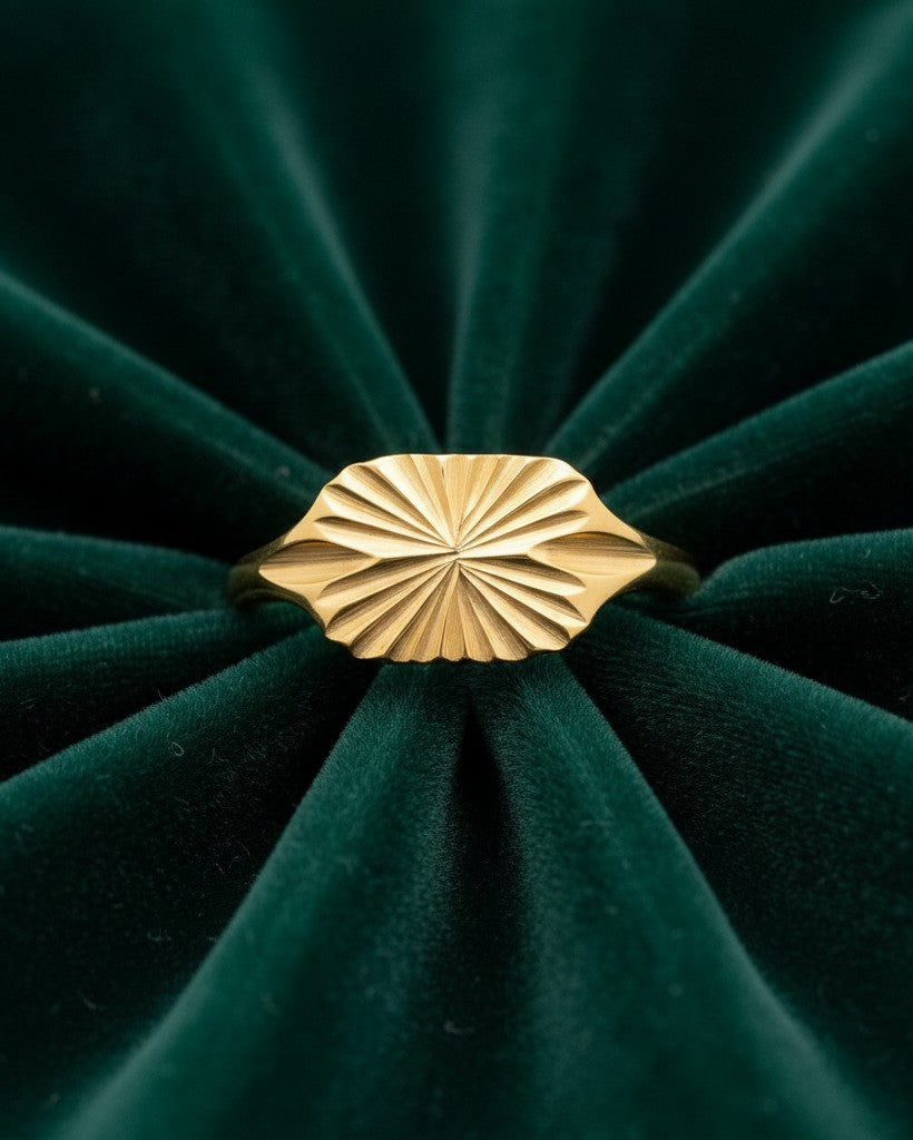 Elli Jewellery gold plated signet ring featuring a carved geometric sunburst design on a dark green velvet background.