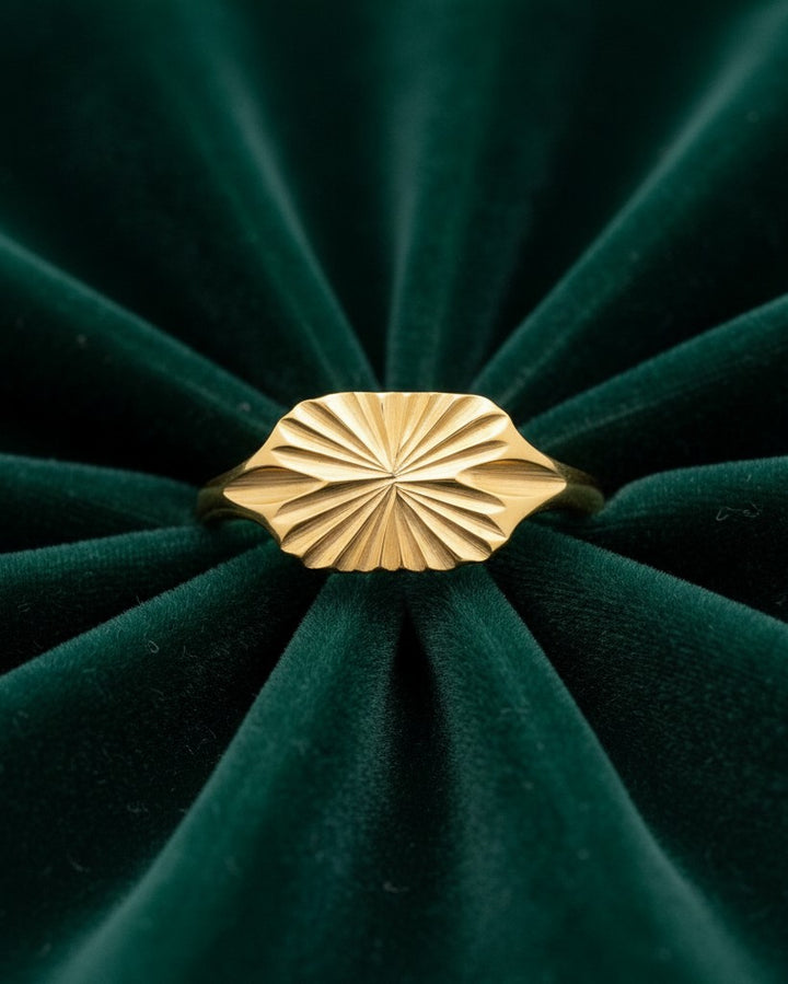 Elli Jewellery gold plated signet ring featuring a carved geometric sunburst design on a dark green velvet background.