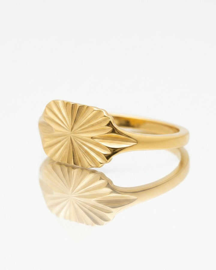 Elli Jewellery gold plated signet ring featuring a carved geometric sunburst design on a reflective white surface