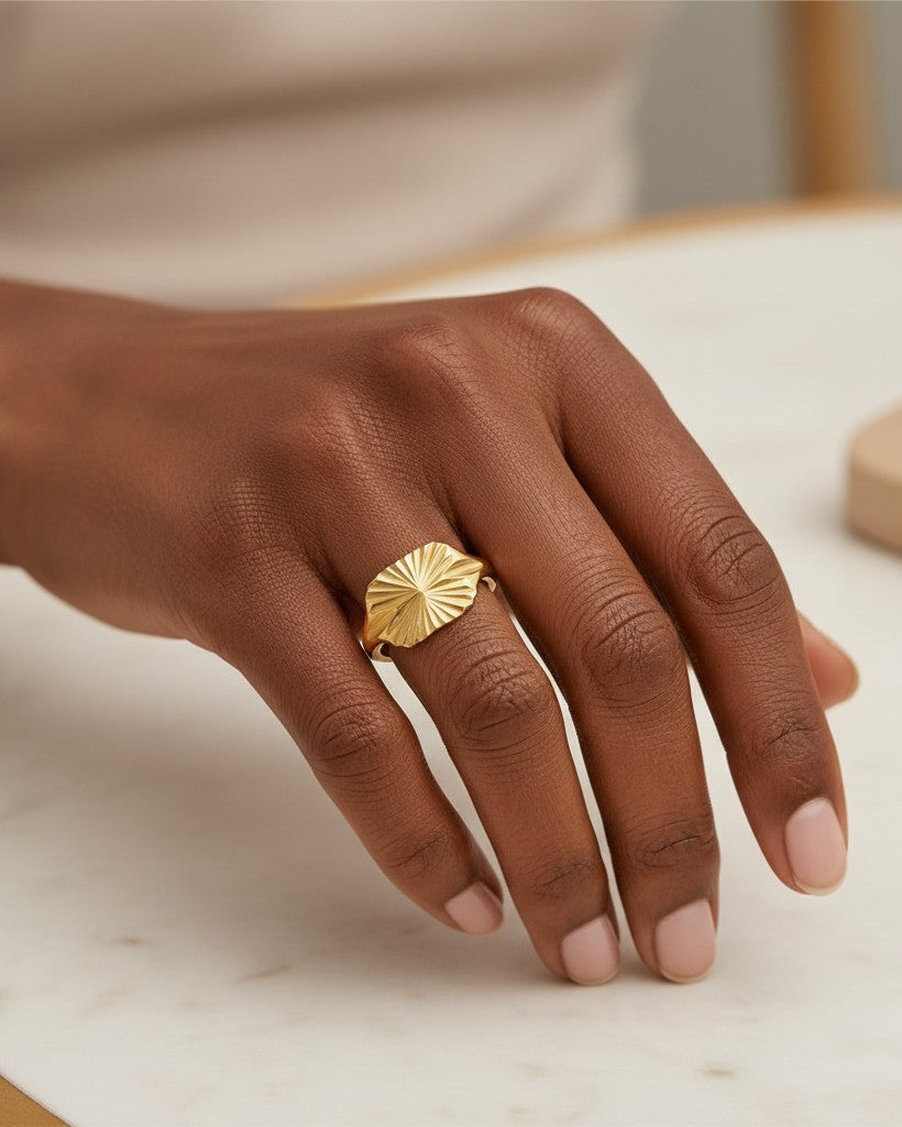 Elli Jewellery gold plated signet ring featuring carved geometric sunburst detailing worn on a model's finger.