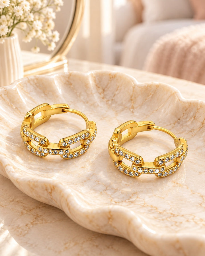 Elli Jewellery gold plated chunky chain link hoop earrings with sparkling crystals resting on a decorative shell dish.