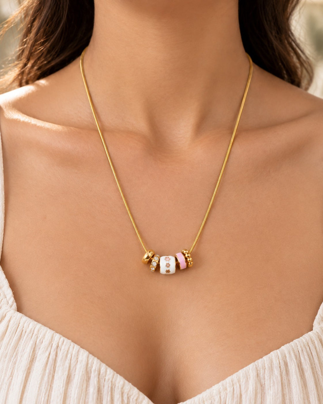 Elli Jewellery gold plated dainty necklace featuring white and pink enamel charms worn on a woman's neck