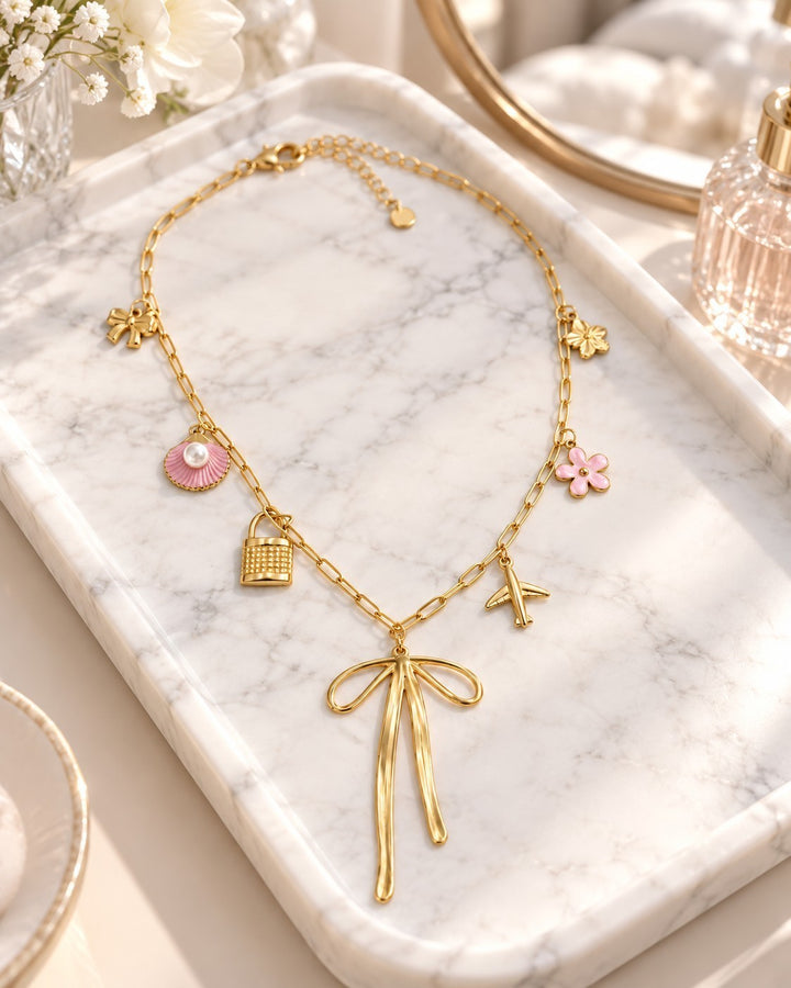 Elli Jewellery gold plated charm necklace featuring a bow, airplane, padlock, and pink enamel flower and shell charms.