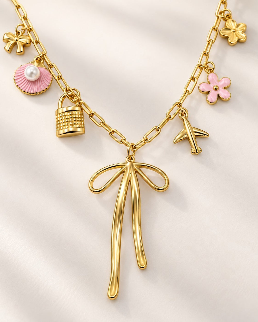 Elli Jewellery gold plated charm necklace featuring a bow pendant, pink shell, padlock, airplane, and flower charms.