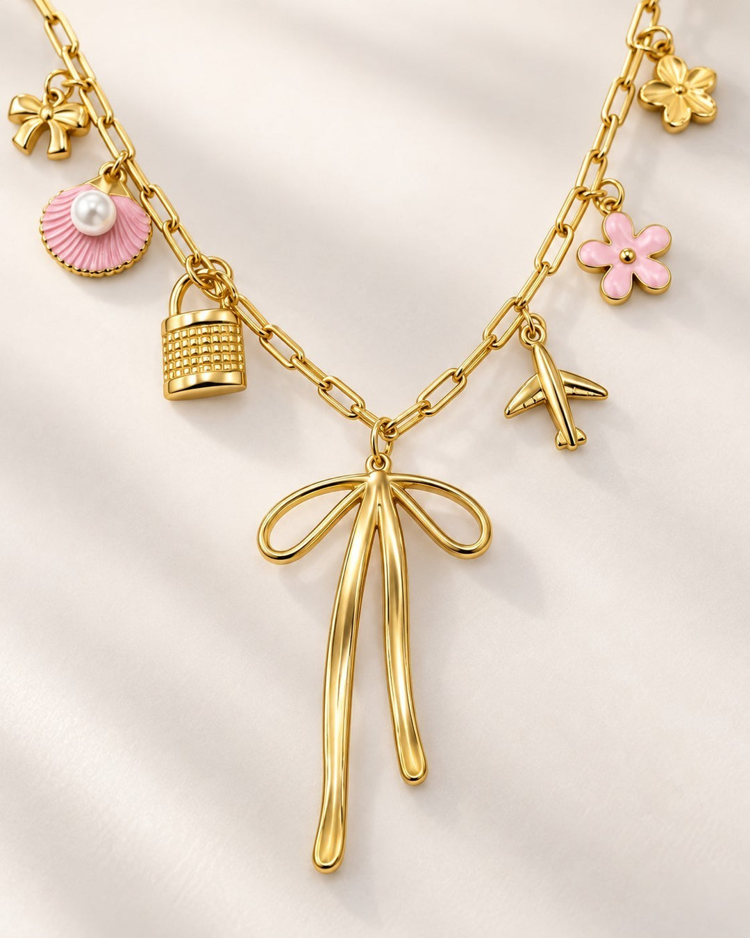 Elli Jewellery gold plated charm necklace featuring a bow pendant, pink shell, padlock, airplane, and flower charms.