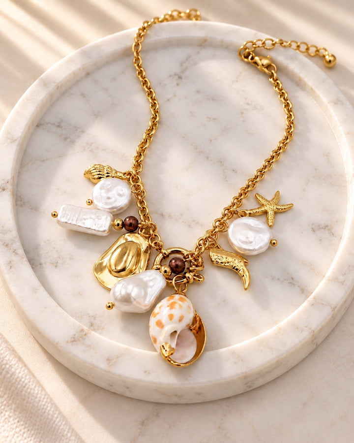 Elli Jewellery gold plated layered necklace featuring assorted seashell, pearl, and starfish charms on a marble tray.
