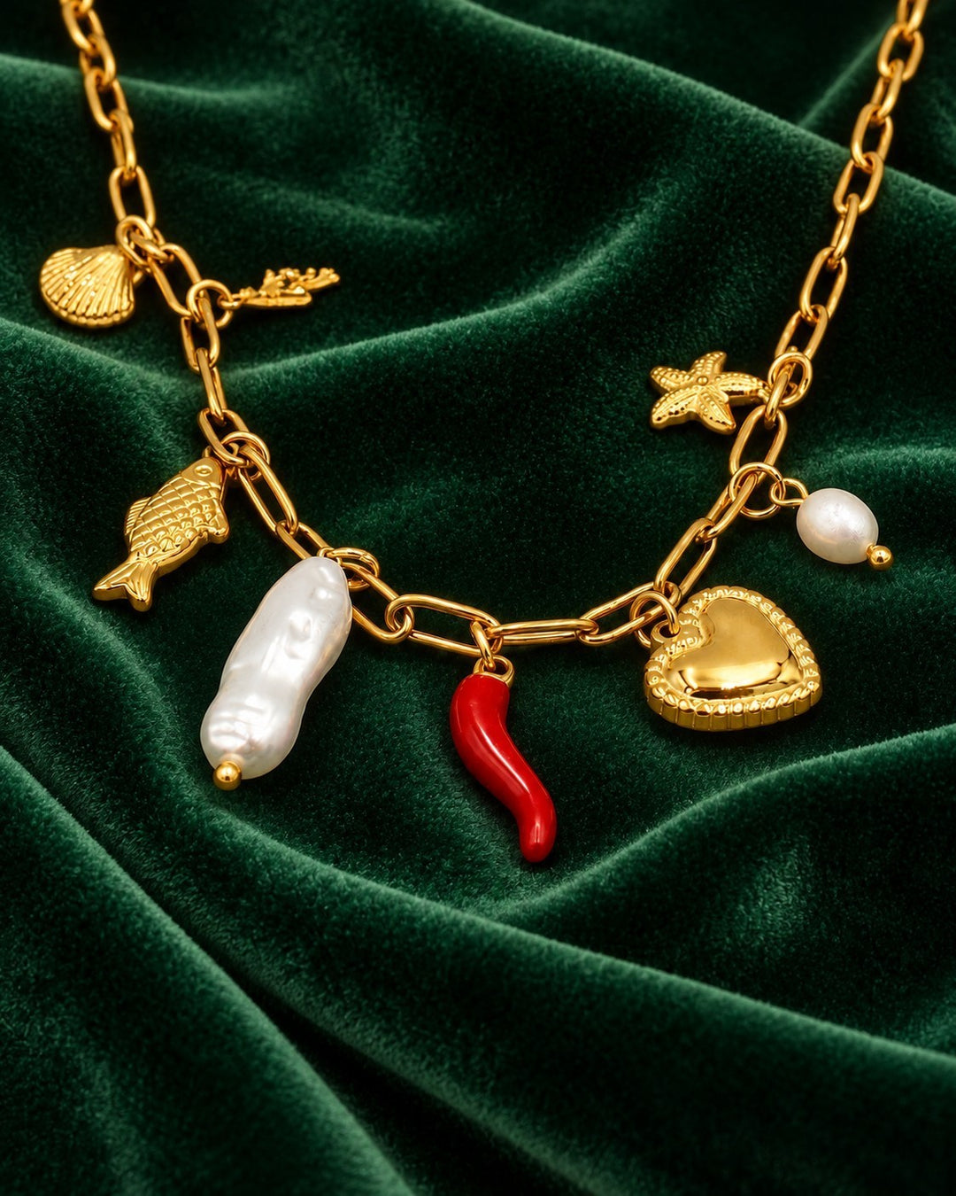 Elli Jewellery gold-plated charm necklace featuring a heart, pearl, red chili, and sea-themed charms on green velvet.