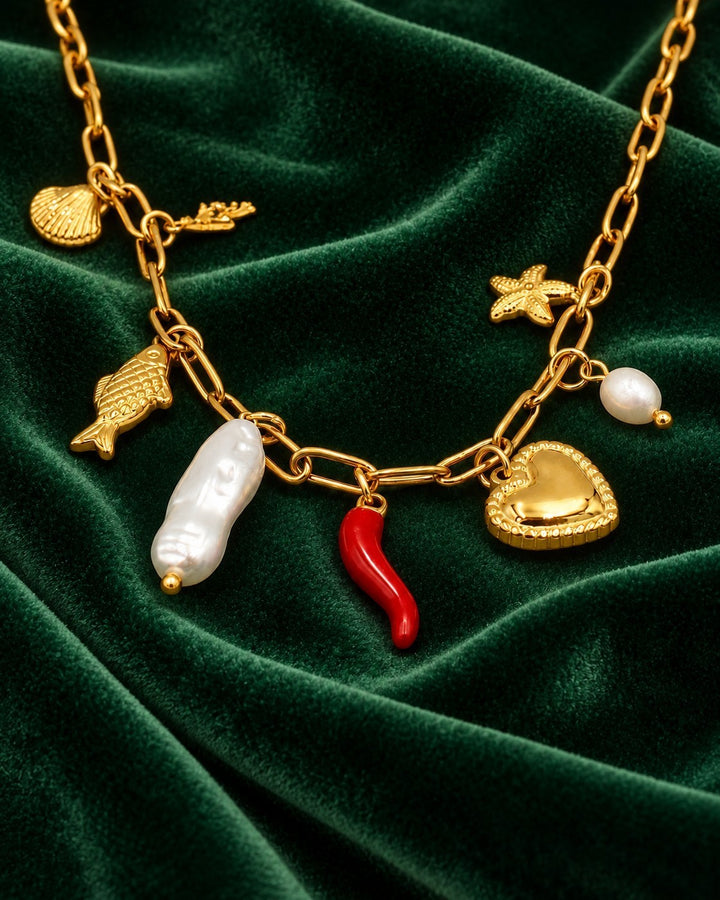 Elli Jewellery gold-plated charm necklace featuring a heart, pearl, red chili, and sea-themed charms on green velvet.