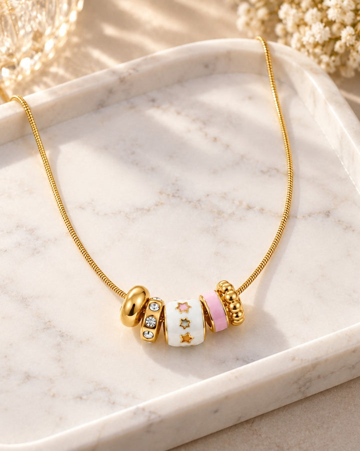 Elli Jewellery gold plated dainty necklace with multi-coloured enamel and crystal charms on a marble tray.