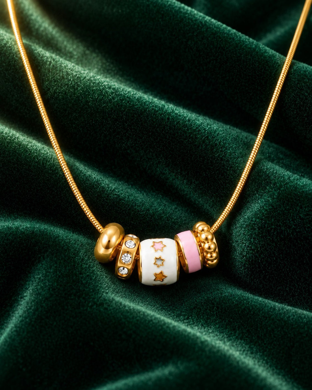 Elli Jewellery gold plated dainty necklace with multi-coloured enamel and crystal charms on a green velvet background