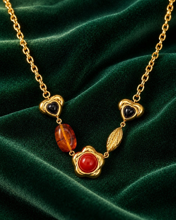 Elli Jewellery gold plated necklace featuring heart, leaf, and flower charms with amber and red stones on green velvet