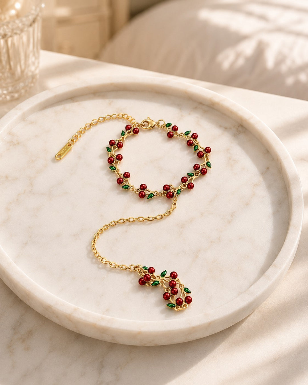 Elli Jewellery gold plated hand chain bracelet featuring delicate red cherry charms and green leaves on a marble tray