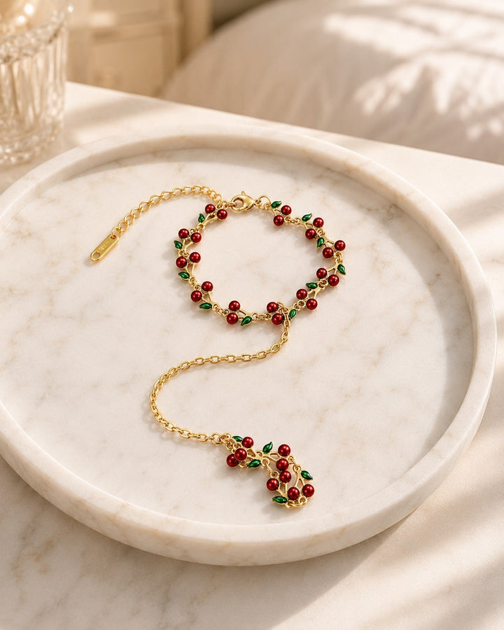 Elli Jewellery gold plated hand chain bracelet featuring delicate red cherry charms and green leaves on a marble tray