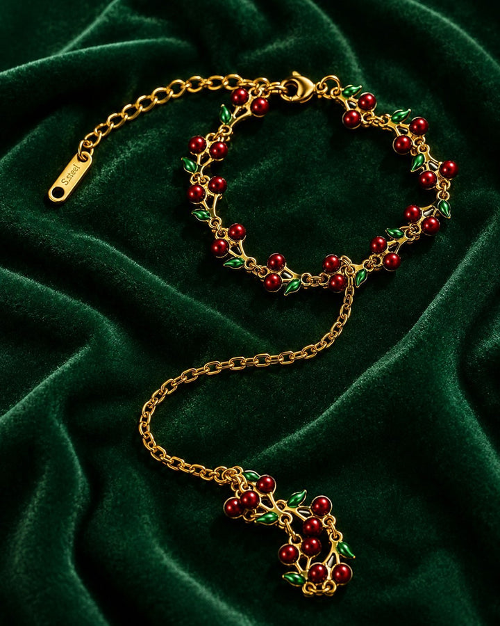 Elli Jewellery gold plated hand chain bracelet featuring red cherry charms and green leaves on dark green velvet