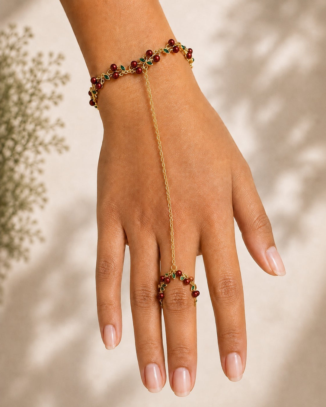Elli Jewellery gold plated hand chain bracelet with red cherry charms and green leaves worn on a woman's hand