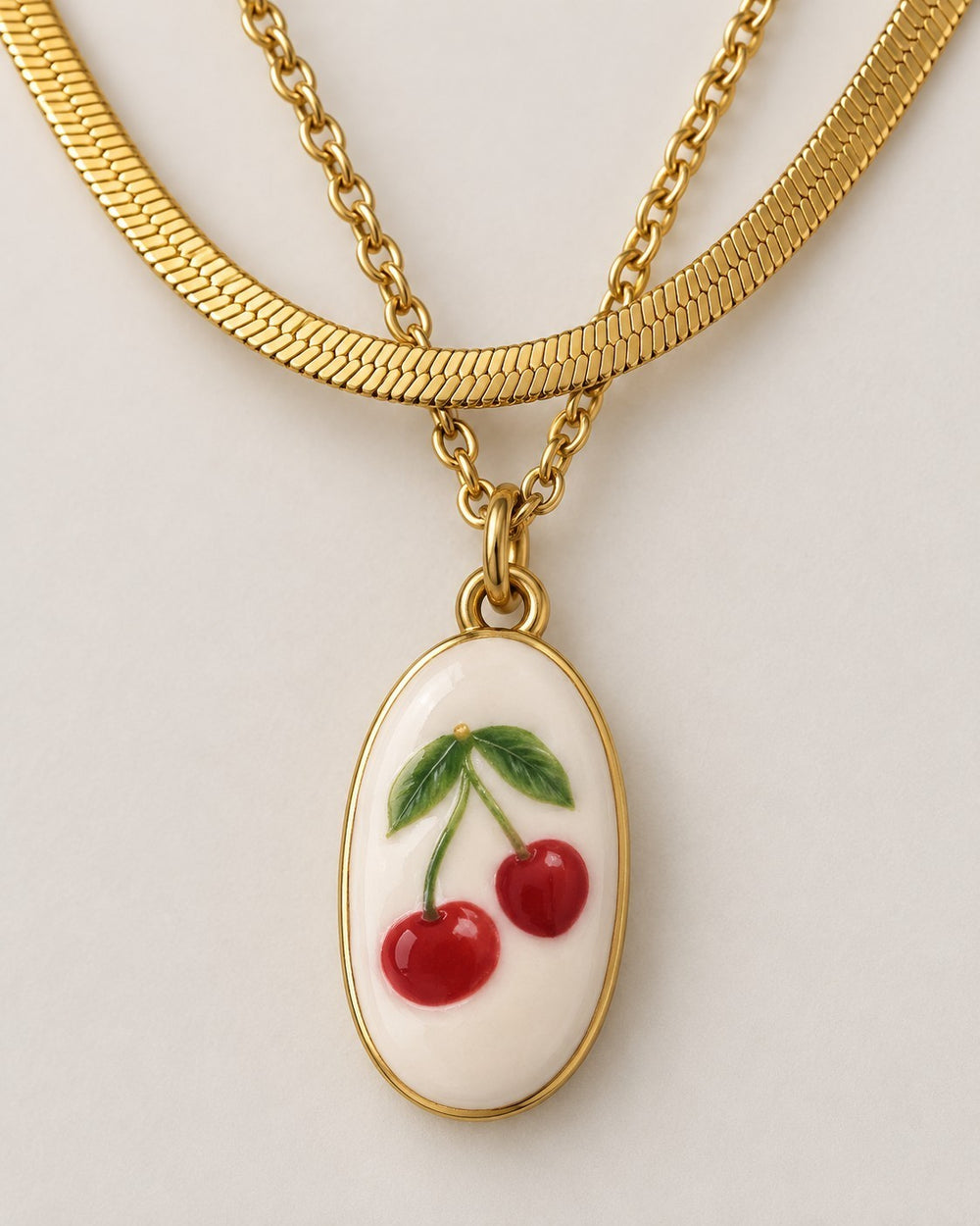 Elli Jewellery gold plated layered snake chain necklace featuring an oval pendant with a red cherry charm design.