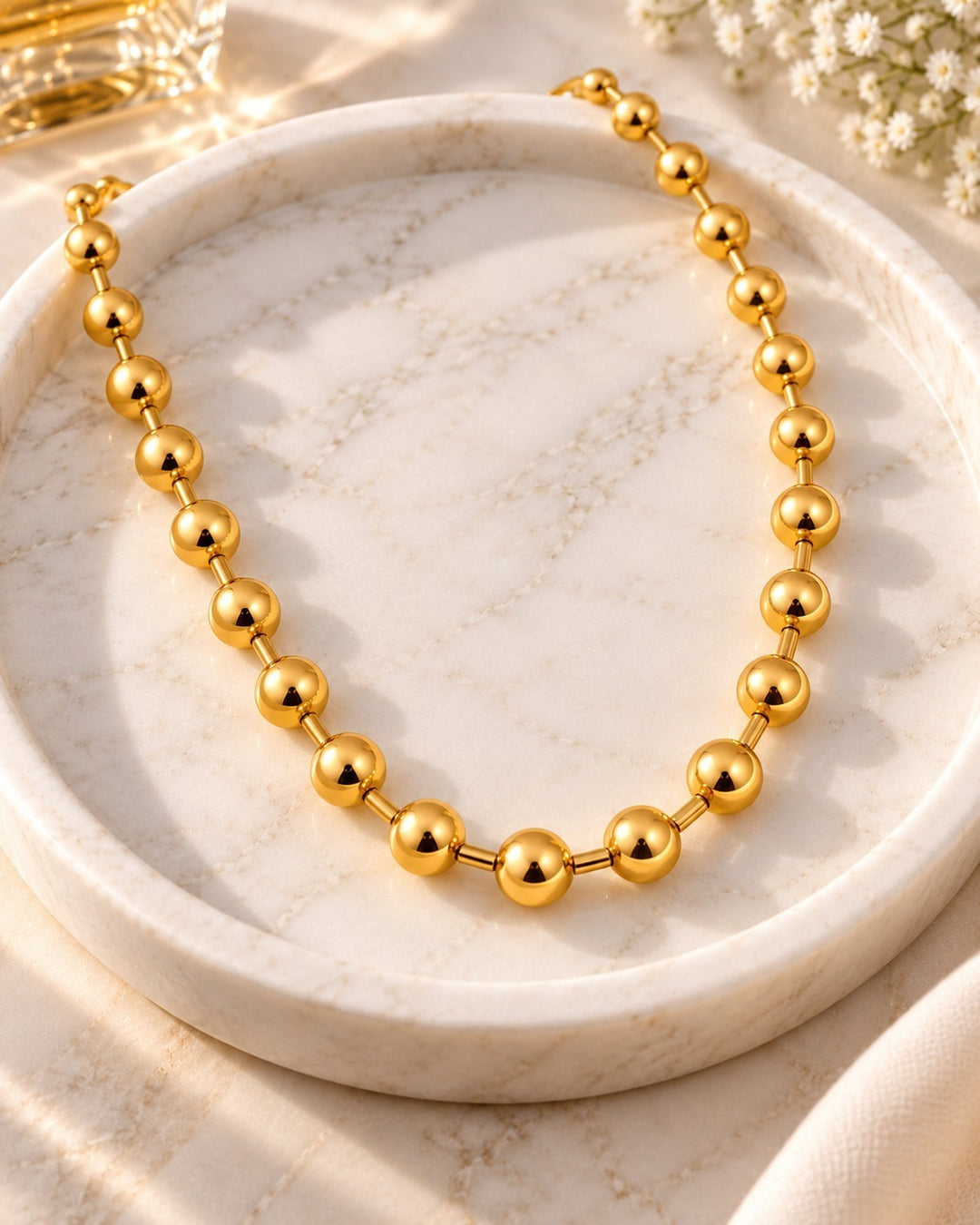 Elli Jewellery gold plated chunky ball chain necklace resting on a white marble tray with soft sunlight.
