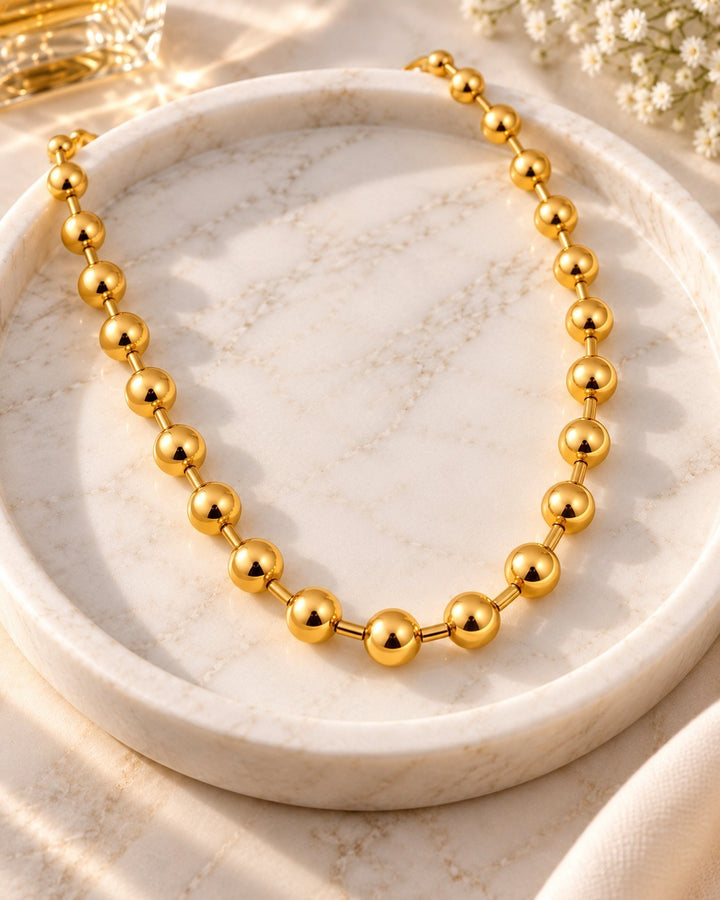 Elli Jewellery gold plated chunky ball chain necklace resting on a white marble tray with soft sunlight.