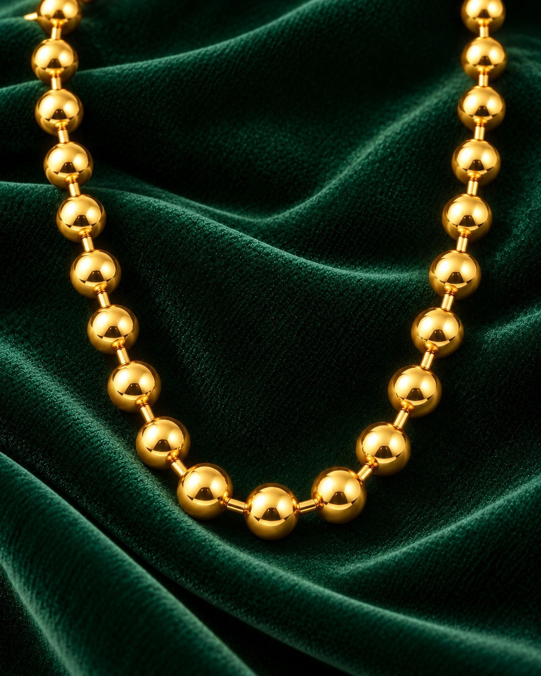 Elli Jewellery gold plated chunky ball chain necklace resting on a luxurious dark green velvet fabric background.
