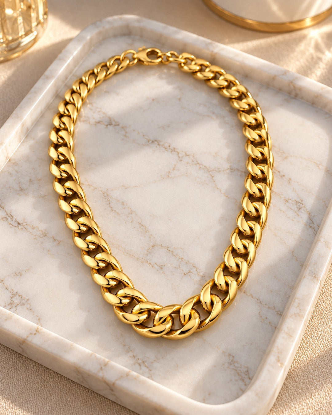 Elli Jewellery gold-plated chunky Cuban chain necklace resting on a marble tray in warm sunlight.