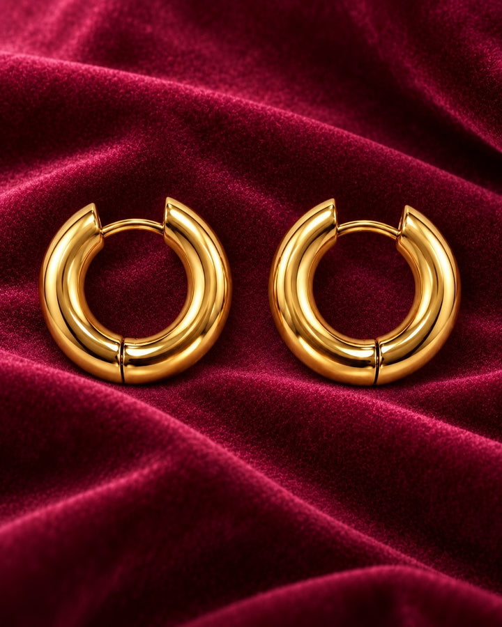 Elli Jewellery gold plated chunky 2cm hoop earrings resting on a luxurious deep red velvet fabric background.