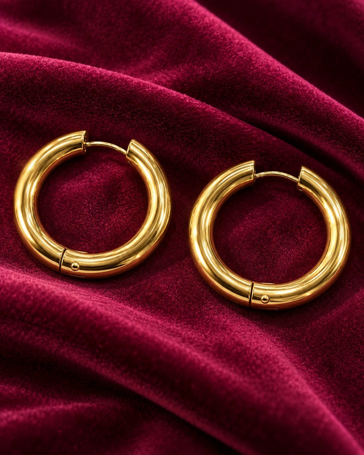 Elli Jewellery 3cm gold plated chunky hoop earrings with a textured surface resting on deep red velvet fabric.