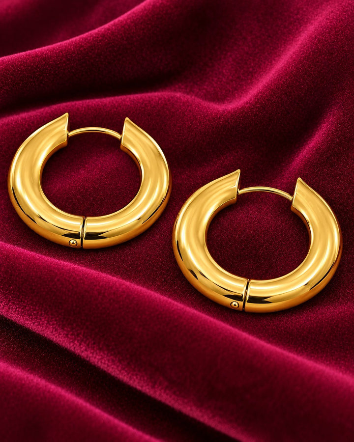 Elli Jewellery gold plated chunky hoop earrings with a polished finish resting on a deep red velvet fabric background.