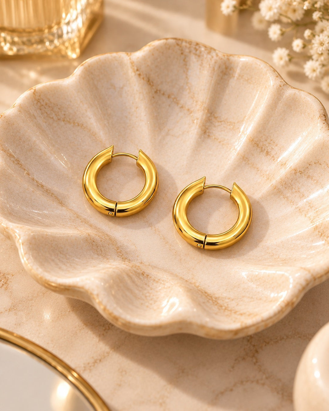 Elli Jewellery gold plated chunky hoop earrings with a smooth polished finish resting on a decorative shell dish
