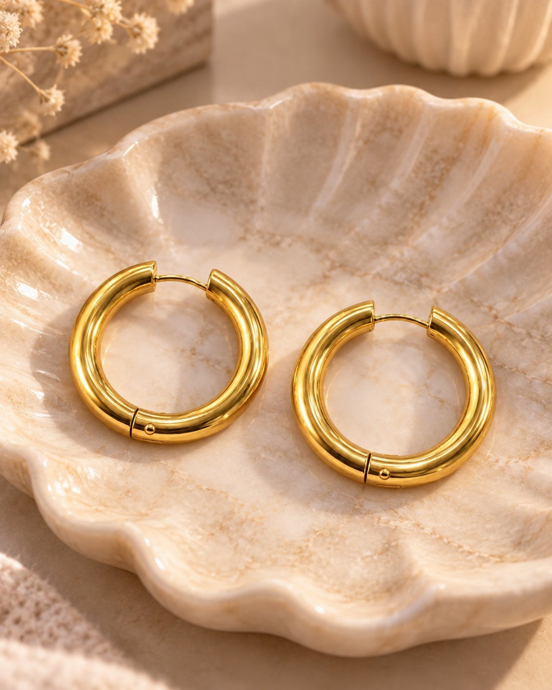 Elli Jewellery 3cm gold plated chunky hoop earrings with a textured surface resting in a decorative shell dish