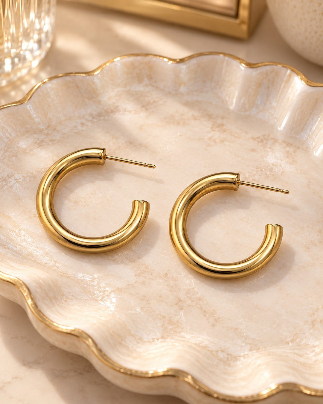 Elli Jewellery gold plated chunky hoop earrings with a polished finish resting on a decorative scalloped tray.