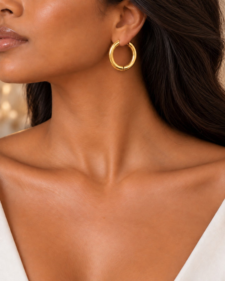 Elli Jewellery gold plated chunky huggie hoop earrings worn by a model with dark hair.