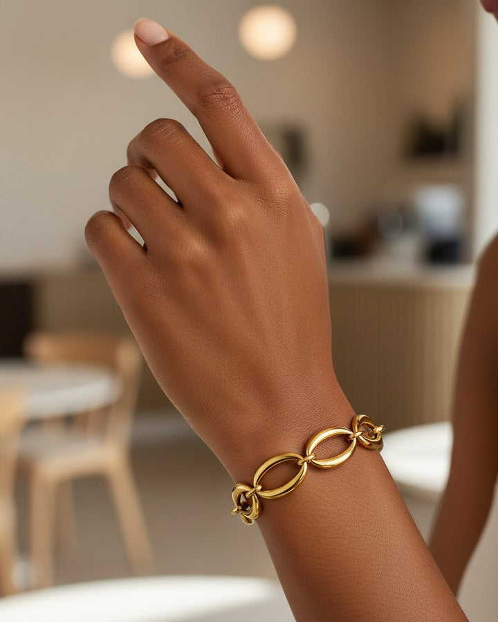 Elli Jewellery gold plated chunky link chain bracelet worn on a woman's wrist in a bright, modern interior.