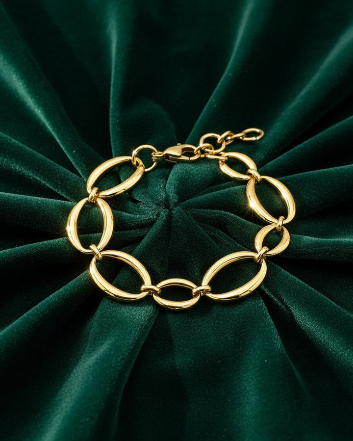 Elli Jewellery gold plated chunky link chain bracelet resting on a luxurious dark green velvet background.