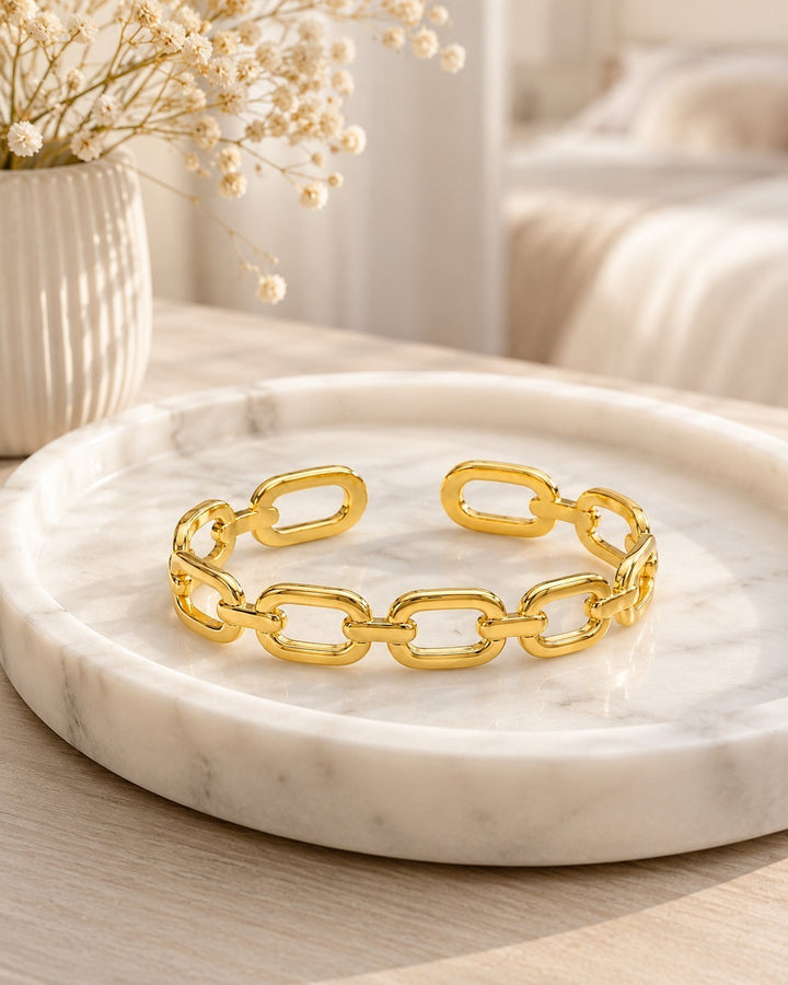 Elli Jewellery gold plated chunky link chain cuff bangle resting on a white marble tray with dried flowers.