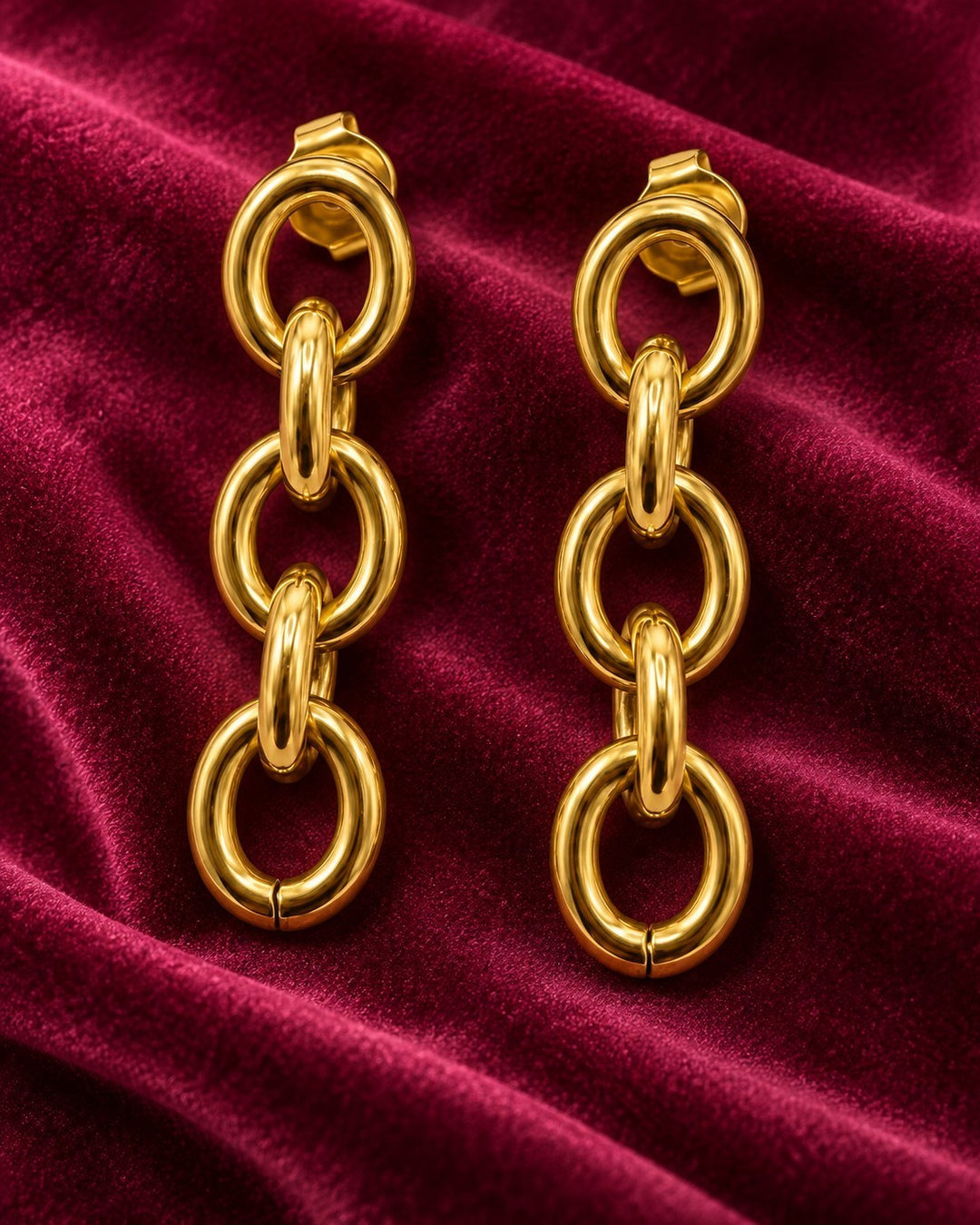 Elli Jewellery gold plated chunky link chain drop earrings on a deep red velvet background
