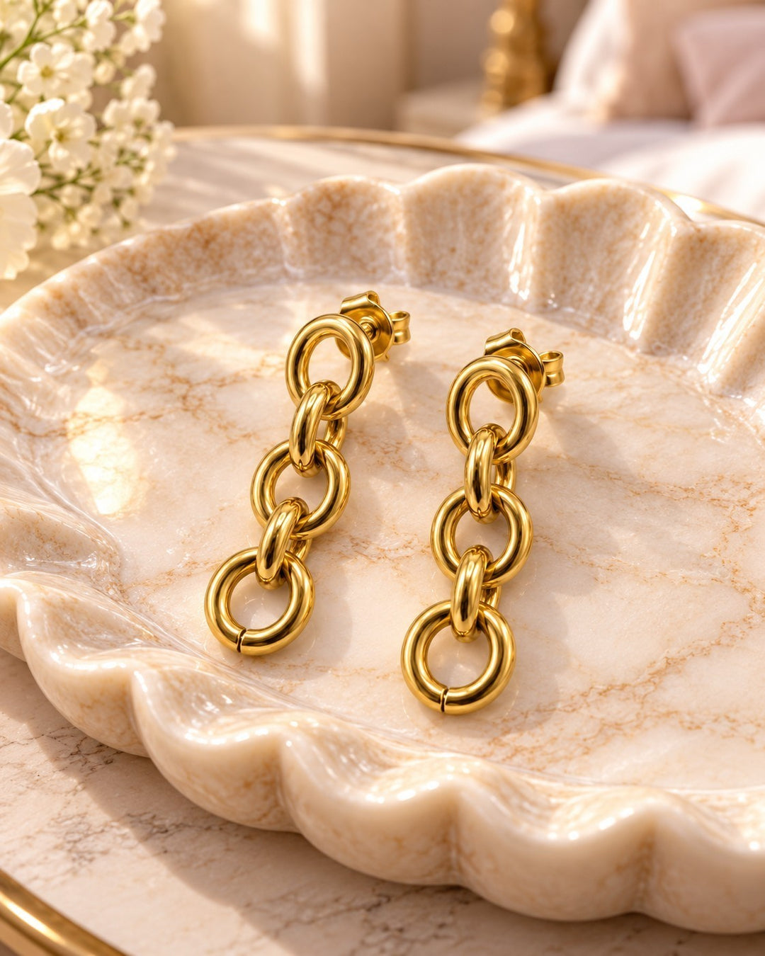 Elli Jewellery gold plated chunky link chain drop earrings resting on a decorative scalloped marble dish