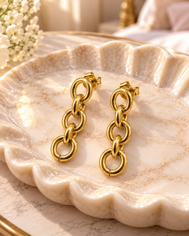 Elli Jewellery gold plated chunky link chain drop earrings resting on a decorative scalloped marble dish