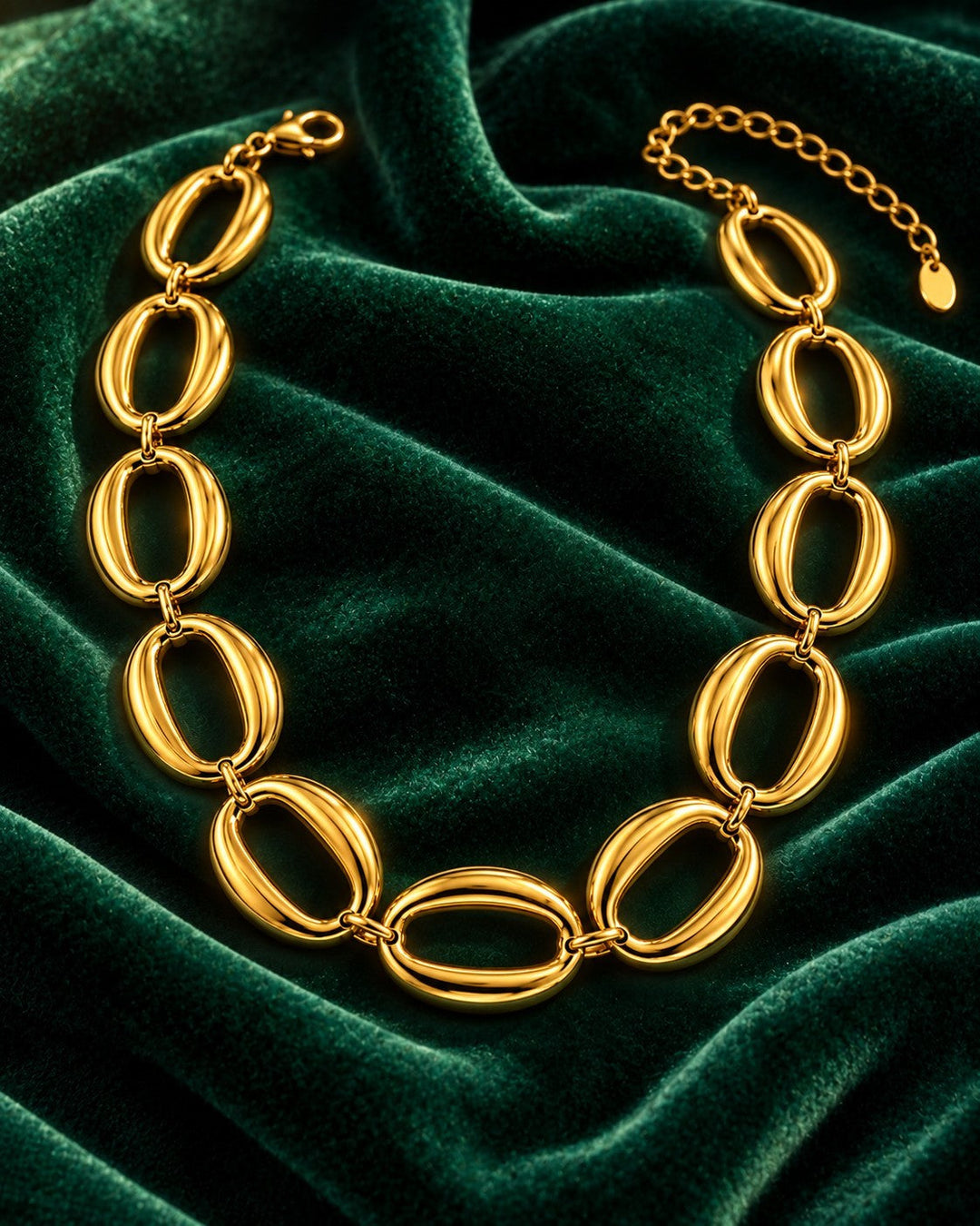Elli Jewellery gold plated chunky oval link chain necklace displayed on a rich dark green velvet background.