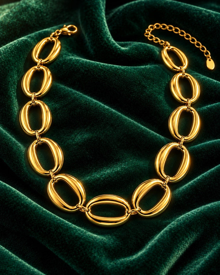 Elli Jewellery gold plated chunky oval link chain necklace displayed on a rich dark green velvet background.