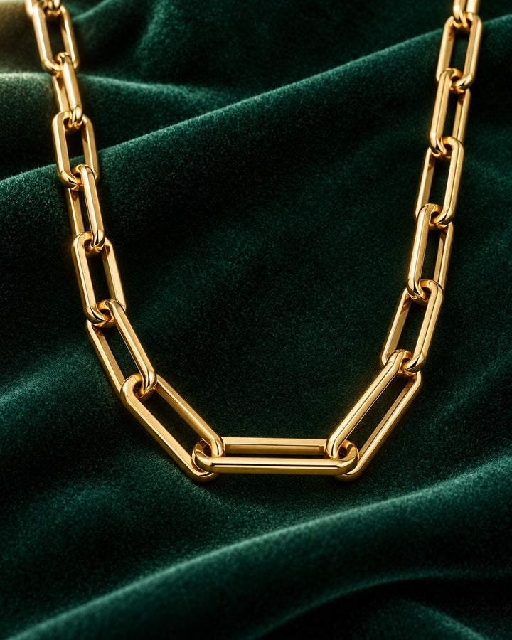 Elli Jewellery gold plated chunky paper link chain necklace resting on a luxurious dark green velvet fabric background.